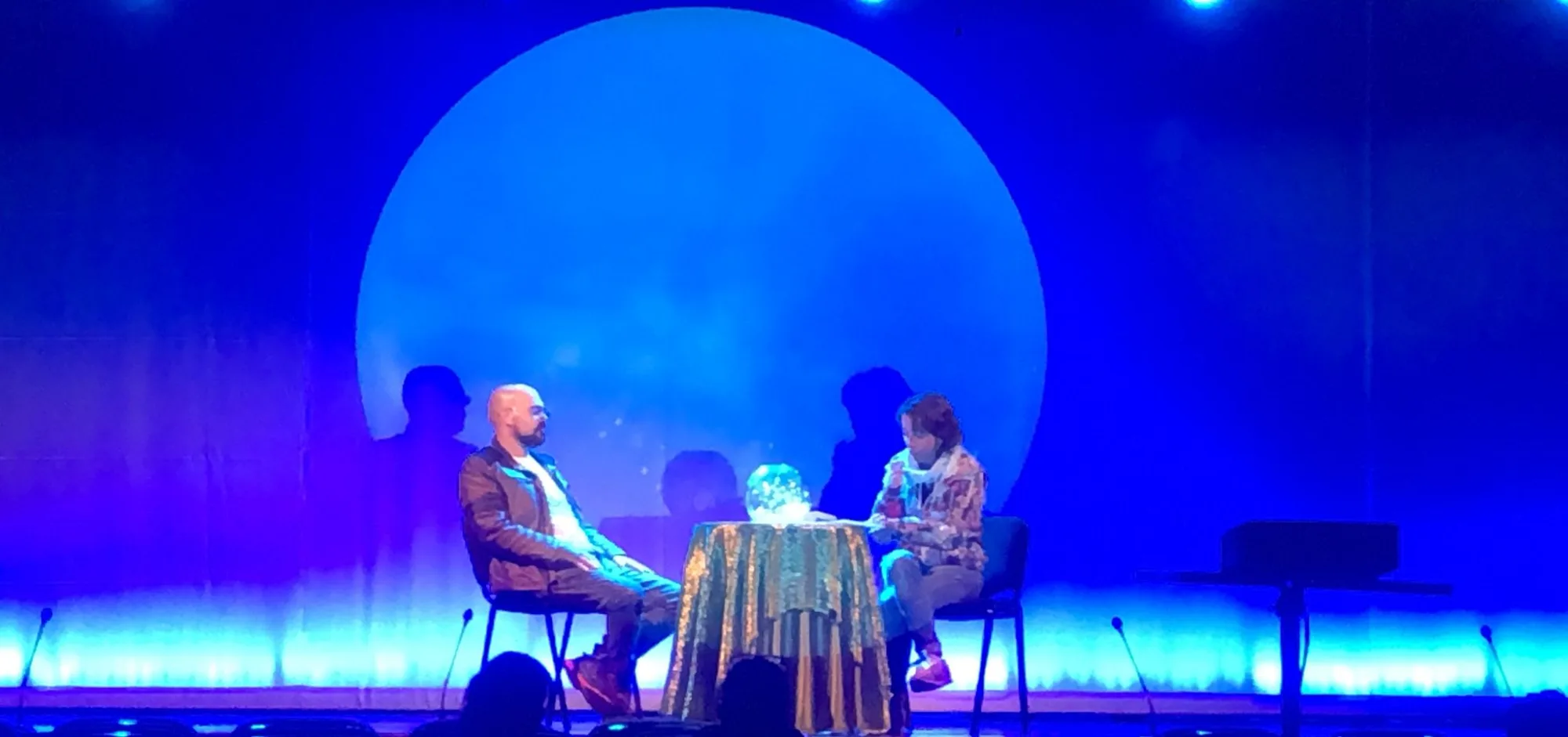 Escena teatral iluminada en azul con una gran luna proyectada al fondo