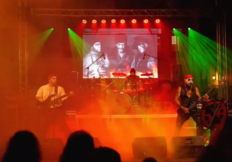 Grupo de rock en escena con luces verdes, humo rojo y una pantalla de vídeo al fondo