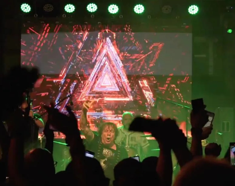 Pantalla LED con un triángulo de luz detrás del cantante y el público con los brazos en alto